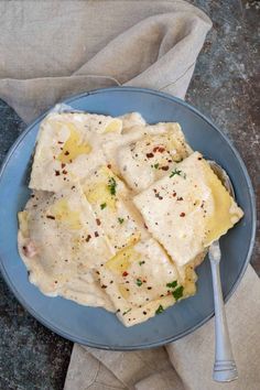 a blue plate topped with ravioli covered in cheese and seasoning next to a fork