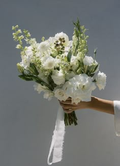 a bouquet of white flowers being held by a woman's hand in front of a gray background