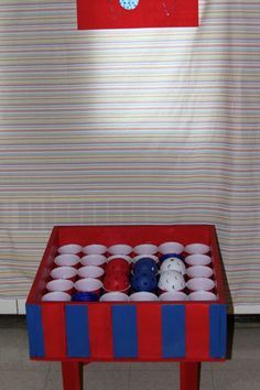 a red table topped with lots of cups filled with white and blue items in front of a striped wall