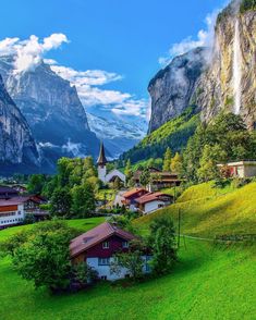 the village is surrounded by mountains and green grass, with houses in the foreground