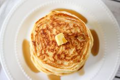 a stack of pancakes on a white plate with butter and syrup in the middle, ready to be eaten