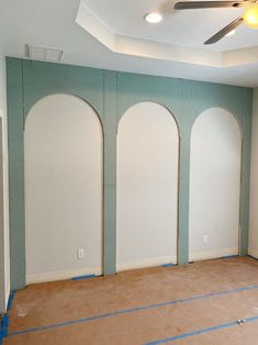 an empty room with three arched windows in the wall and blue tape on the floor