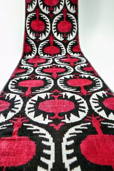 a large red and black rug with white designs on the top, sitting in front of a white wall