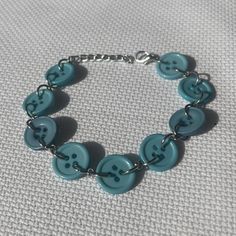 a bracelet with blue buttons and silver chains on a white cloth covered surface, the beads are shaped like skulls