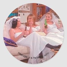 two women in wedding dresses sitting on a couch drinking beer and talking to each other