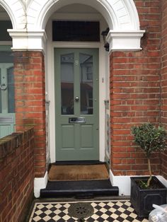 a green front door with two planters on the side and a black and white checkerboard floor