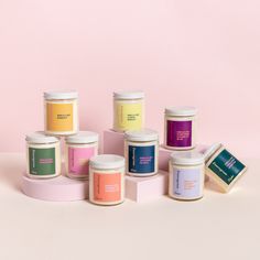 several different types of candles sitting next to each other on a pink surface with one candle in the middle