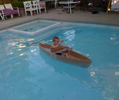 a young boy is sitting in a small boat on the pool's edge while holding a paddle