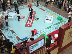 a group of people standing around a monopoly board game on display at a convention center