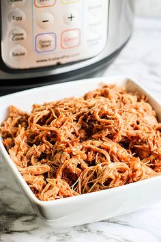 shredded meat in a white bowl next to an instant pot