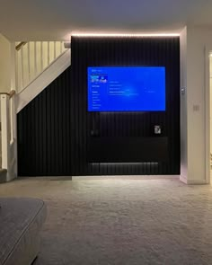 a living room with a large screen on the wall and stairs leading up to it