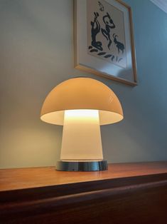 a mushroom lamp sitting on top of a wooden table next to a framed artwork above it