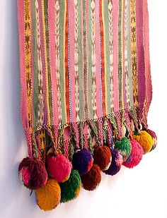 a multicolored wall hanging with tassels and pom - poms