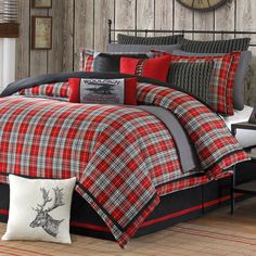 a red and black plaid comforter set with deer head on the pillow, in front of a wooden paneled wall