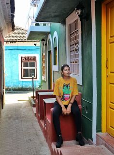 a woman sitting on the steps in front of a building with yellow doors and windows