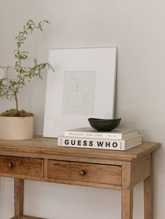 a wooden table topped with books and a potted plant next to a white wall