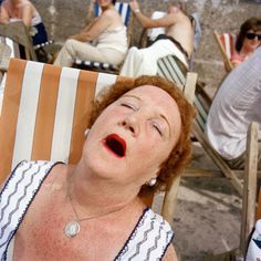 an older woman with red hair sitting in a chair on the beach and looking up