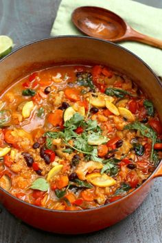 a large pot filled with lots of food on top of a wooden table next to a spoon