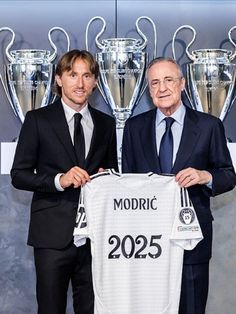 two men standing next to each other in front of trophies and holding a shirt with the number 205 on it