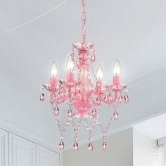 a pink chandelier hanging from the ceiling in a room with white walls and cabinets