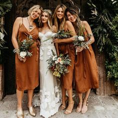 four bridesmaids in brown dresses posing for the camera with greenery around them