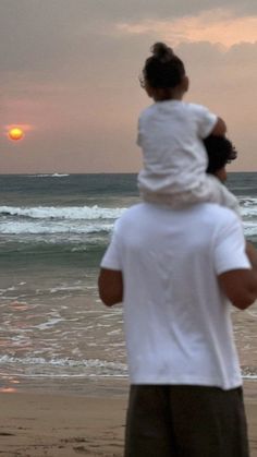 a man holding a child on the beach at sunset