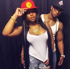 a man and woman standing next to each other in front of a black backdrop wearing gold chains