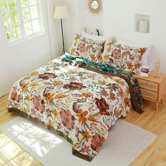 a bed with a floral comforter and matching pillow cases in a white room next to a window