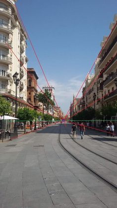 two people walking down the middle of an empty street with buildings on both sides and red tape hanging over them