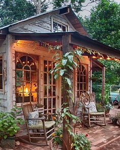 a wooden porch with rocking chairs and lights on the outside, surrounded by greenery