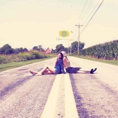 two women sitting on the side of an empty road with their feet up in the air