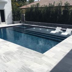 an empty swimming pool in front of a house with white lounge chairs around the pool