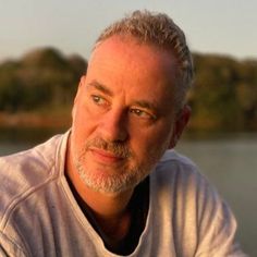 a man with grey hair is sitting by the water