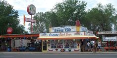 people are standing in front of a small store on the side of the road,