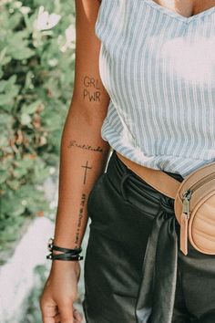 a woman with a cross tattoo on her arm holding a small purse in her hand