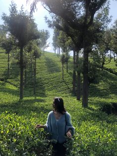 a woman standing in the middle of a lush green field with trees on top of it