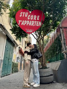 two people standing under a large heart shaped sign