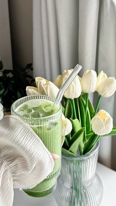 a vase filled with white flowers next to a green smoothie in a glass cup