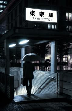 a man with an umbrella walks down the street at night in tokyo station, japan