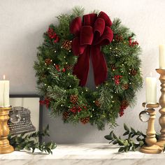 a christmas wreath on a mantle with candles and other holiday decorations around it, all decorated in red velvet bows