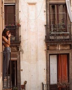 a woman is standing on the balcony talking on her cell phone while looking out at the street