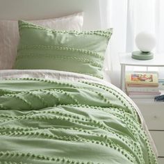 a bed with green comforter and pillows on it next to a nightstand in front of a window