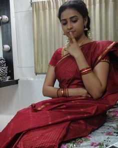 a woman in a red sari sitting on a bed with her hand under her chin