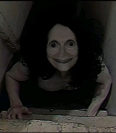 a creepy woman with black hair and big eyes looking at the camera through a hole