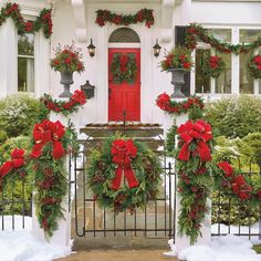 two christmas wreaths on the front gate of a house decorated with red bows and poinsettis