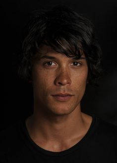 a young man with freckled hair looks at the camera while wearing a black t - shirt