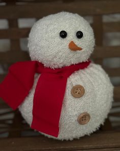 a snowman sitting on top of a wooden bench with a red scarf around it's neck