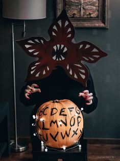 a woman holding a carved pumpkin with letters written on it in front of her face