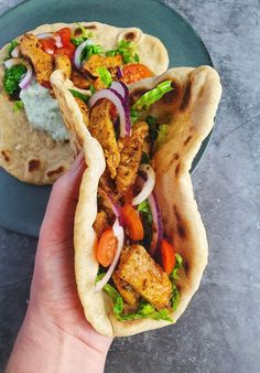 a hand holding a pita filled with chicken and veggies on top of a plate