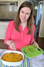 a woman sitting at a table in front of a bowl of food and cutting board